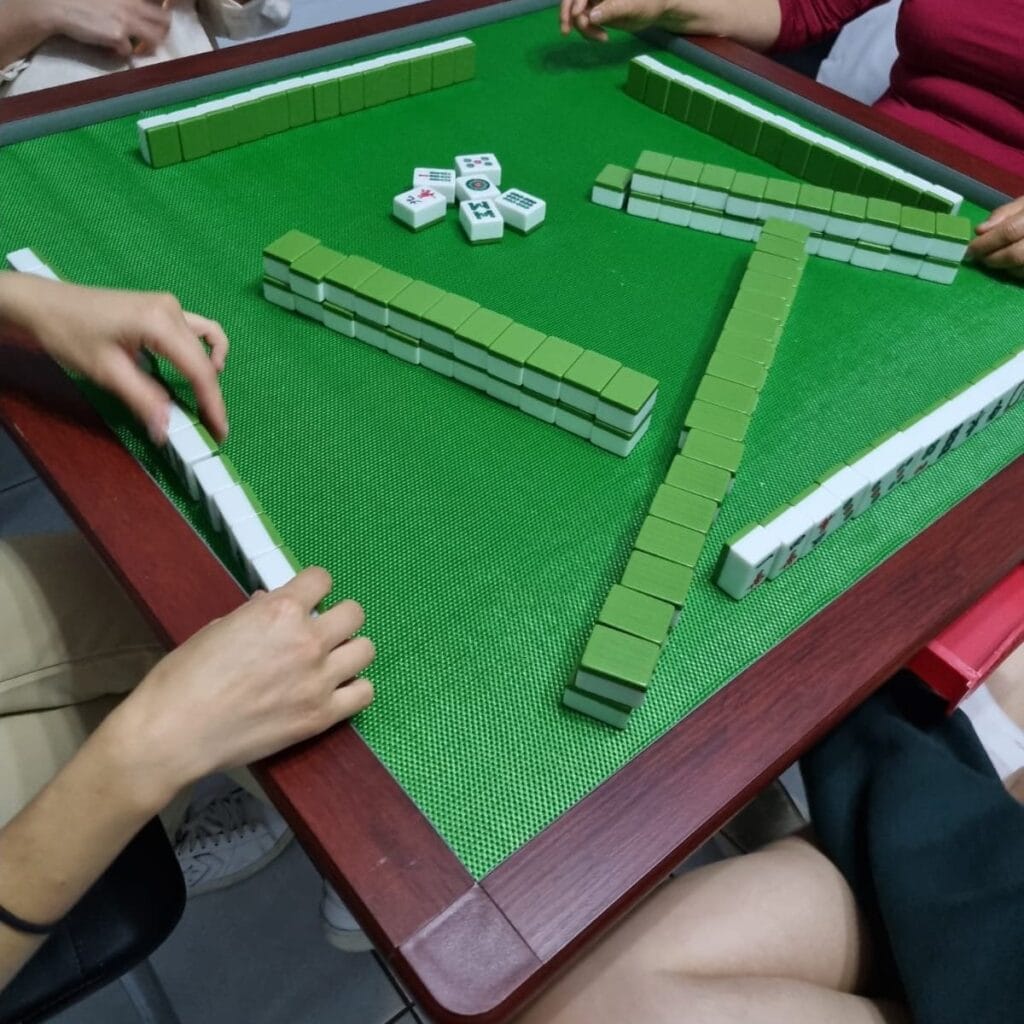 Four players building the wall around a green mahjong table at the start of a game
