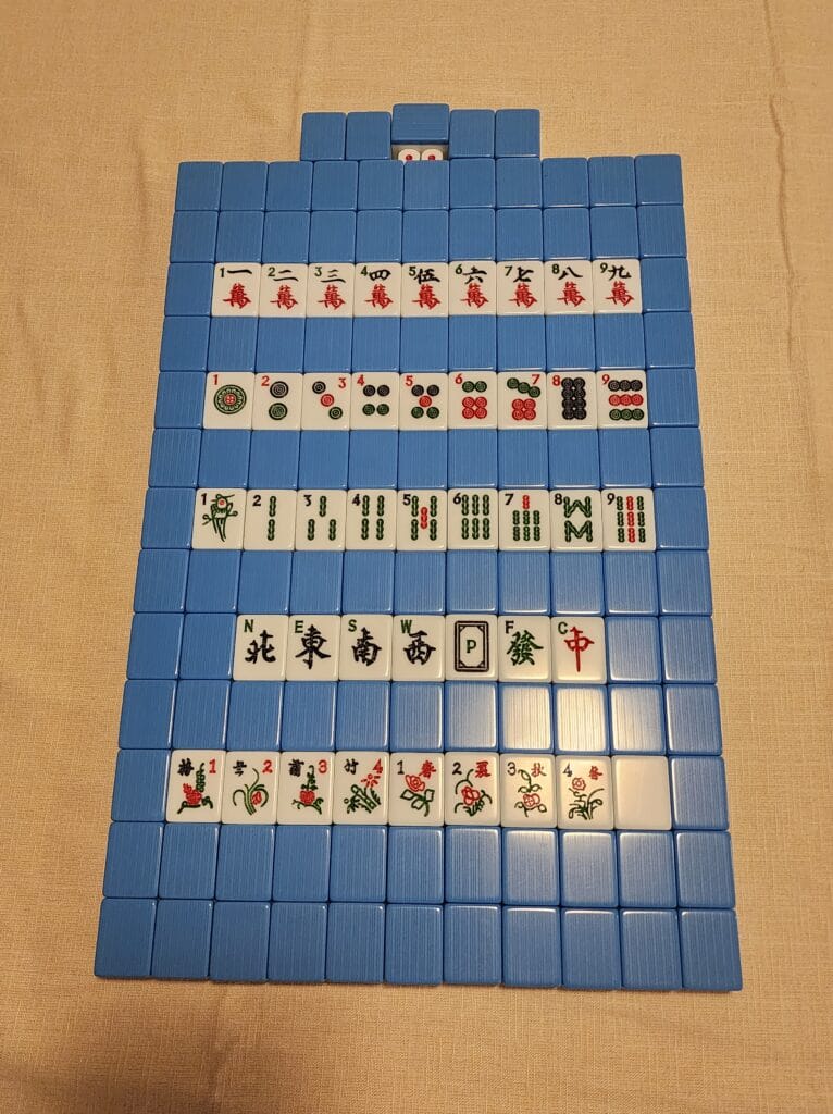 A complete mahjong set laid out face up in rows: characters, circles, bamboo, winds, dragons, flowers and seasons