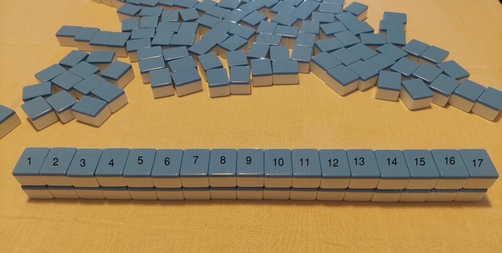 Tiles shuffled face down in a pile beside a row of seventeen tiles being built into the wall